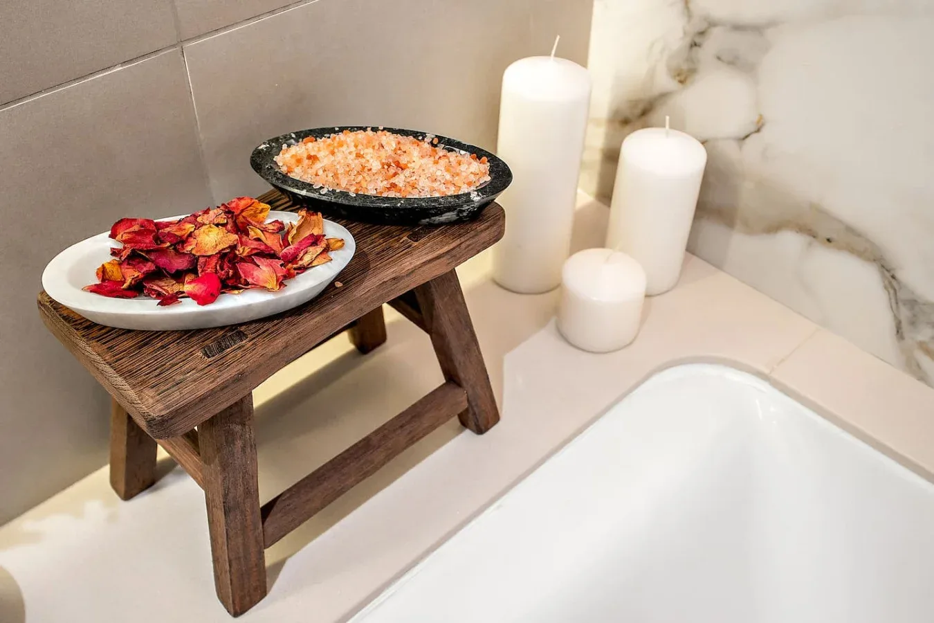 Una bañera junto a un taburete de madera con cuencos de pétalos y sales de baño.