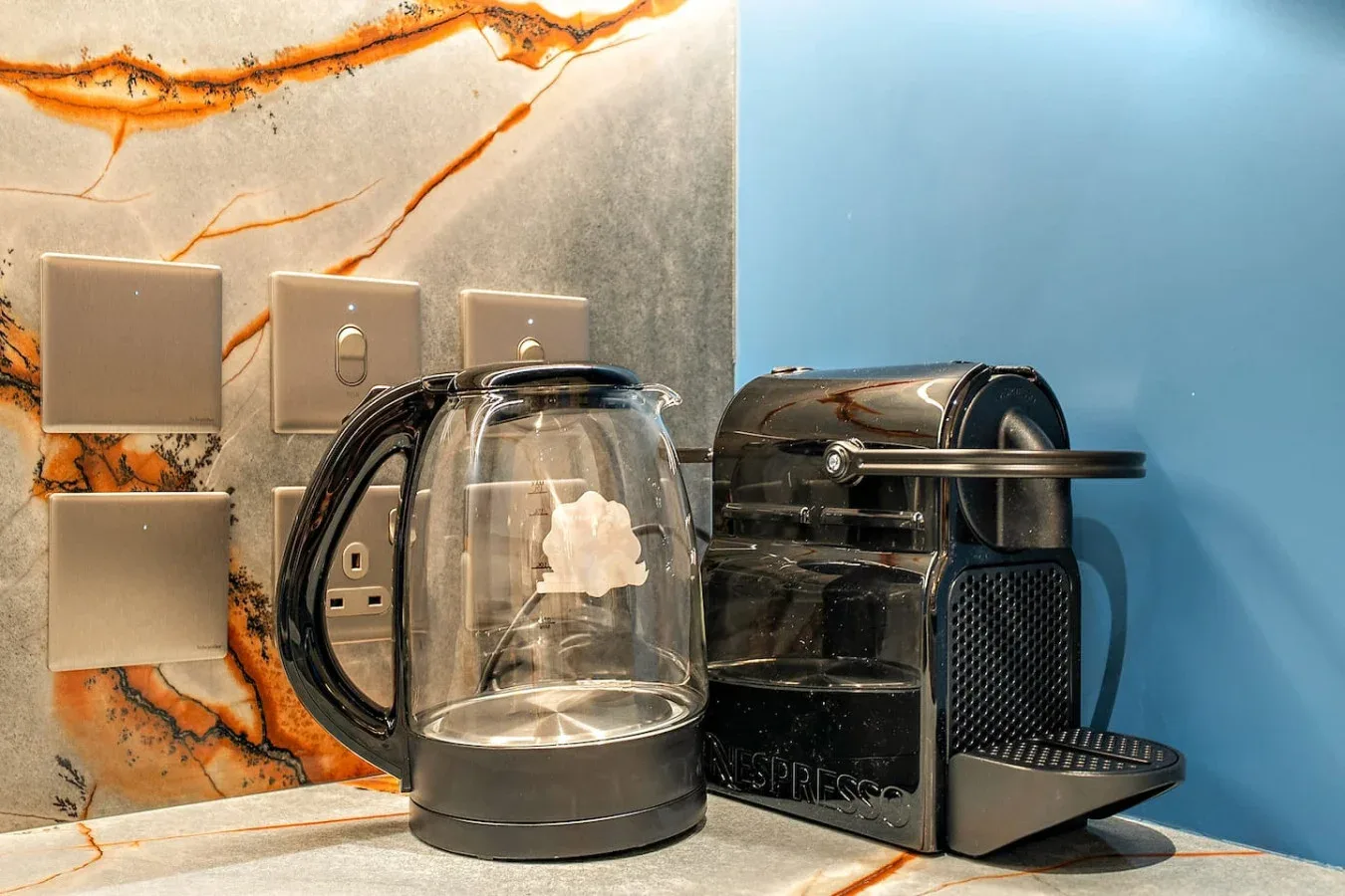 Una estación de café sobre la encimera con una tetera de vidrio y una cafetera espresso.