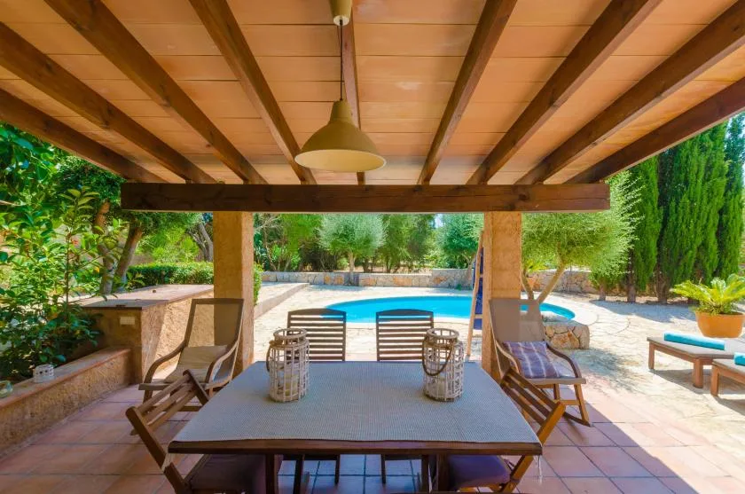 A shaded patio dining area overlooks a swimming pool and garden.