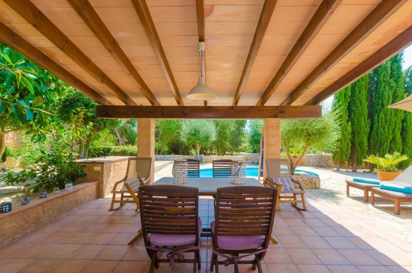 A shaded outdoor patio with a dining table and seating overlooks a swimming pool.