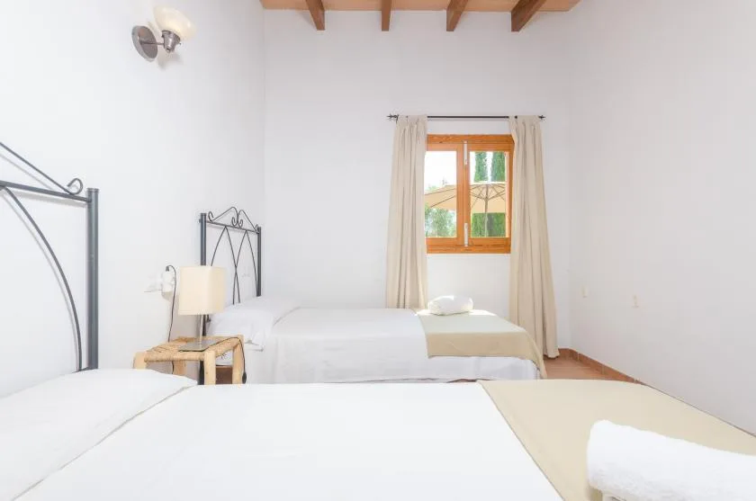 A bright bedroom with beds, light curtains, and a wood-framed window.