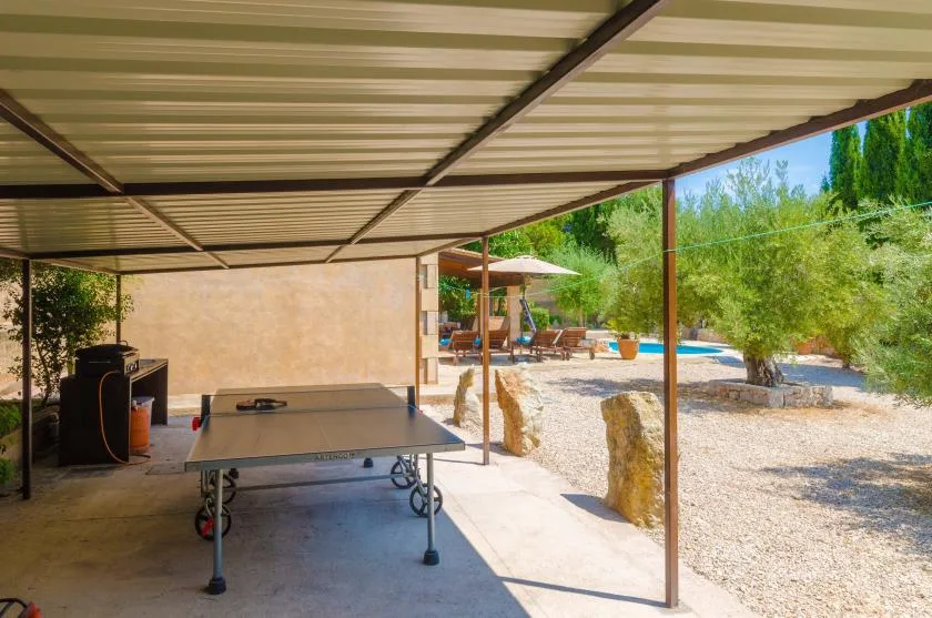 A covered outdoor recreation area with a ping-pong table beside a sunny garden.