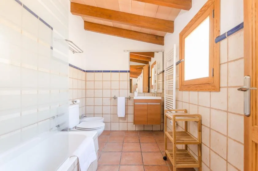 A tiled bathroom with a bathtub, toilet, and wooden vanity.