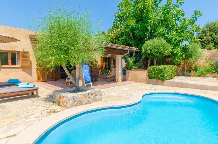 An outdoor swimming pool beside a patio and a tan-colored house.