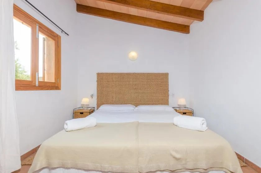 A bedroom with a bed, woven headboard, and wood-framed window.