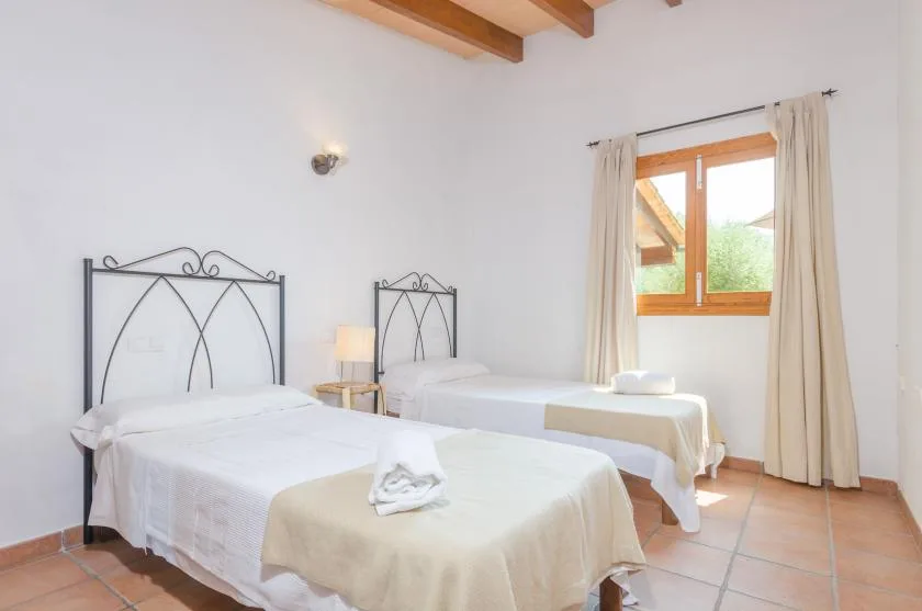 A bright bedroom with two beds and a window framed by curtains.