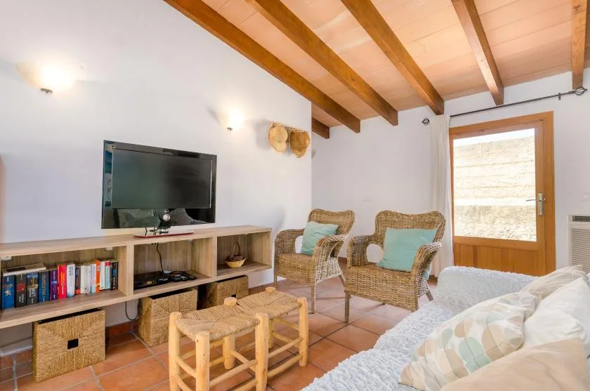A living room with wicker seating, a television, and exposed wooden ceiling beams.