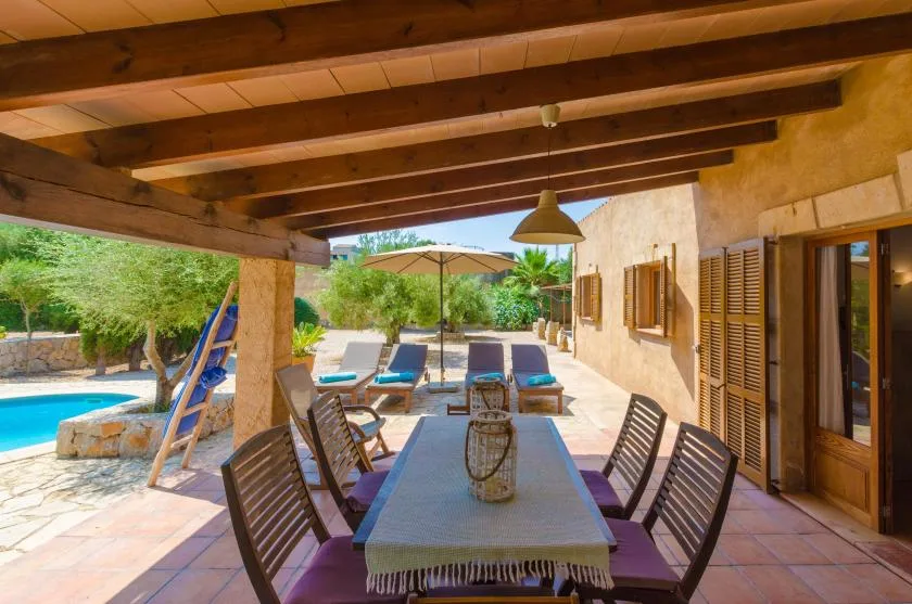 A shaded outdoor dining area with a long table beside a swimming pool.