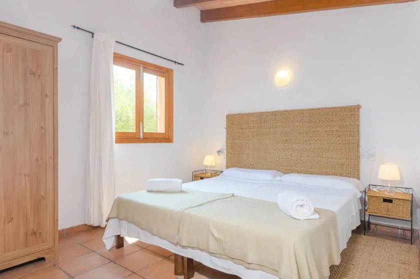 A bright bedroom with a double bed, woven headboard, and wooden window.