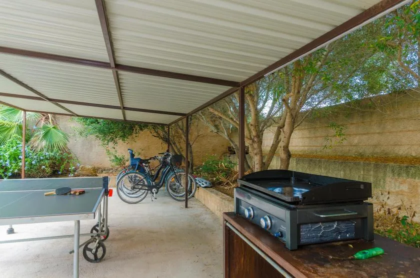 A covered outdoor recreation area with a ping-pong table, bicycles, and a grill.