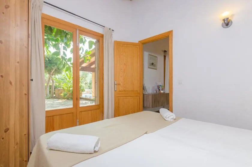 A bedroom with a bed beside wooden-framed glass doors overlooking greenery.