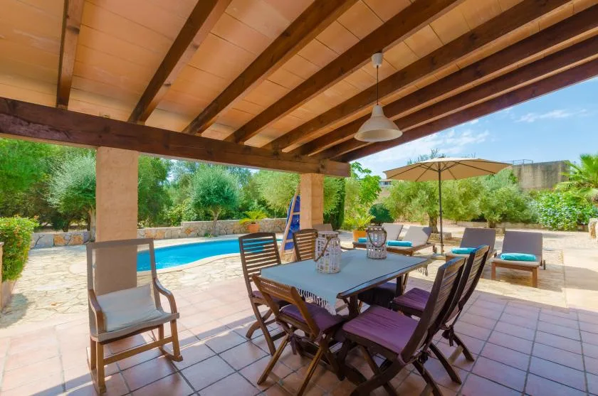 A covered outdoor dining area overlooks a swimming pool and garden.