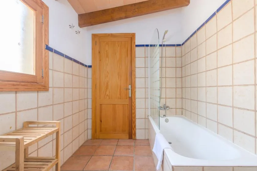 A tiled bathroom with a bathtub, wooden door, and window.