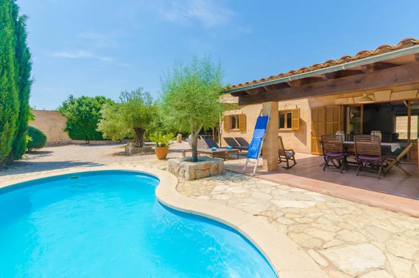 A swimming pool beside a stone patio and a shaded outdoor seating area.