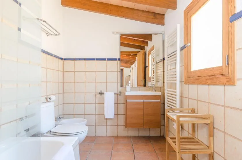 A tiled bathroom with a sink, toilet, and window.