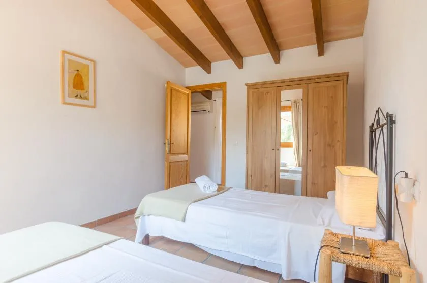A bedroom with two beds and a wooden wardrobe beneath exposed ceiling beams.