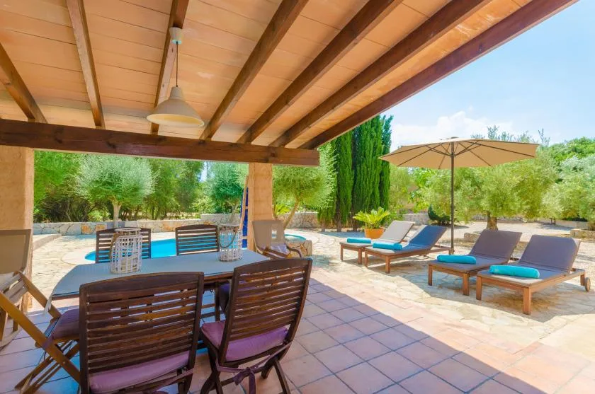 A covered patio with outdoor seating overlooks a swimming pool and lounge area.