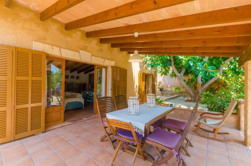 A covered patio with a dining table and chairs opens onto a leafy garden.