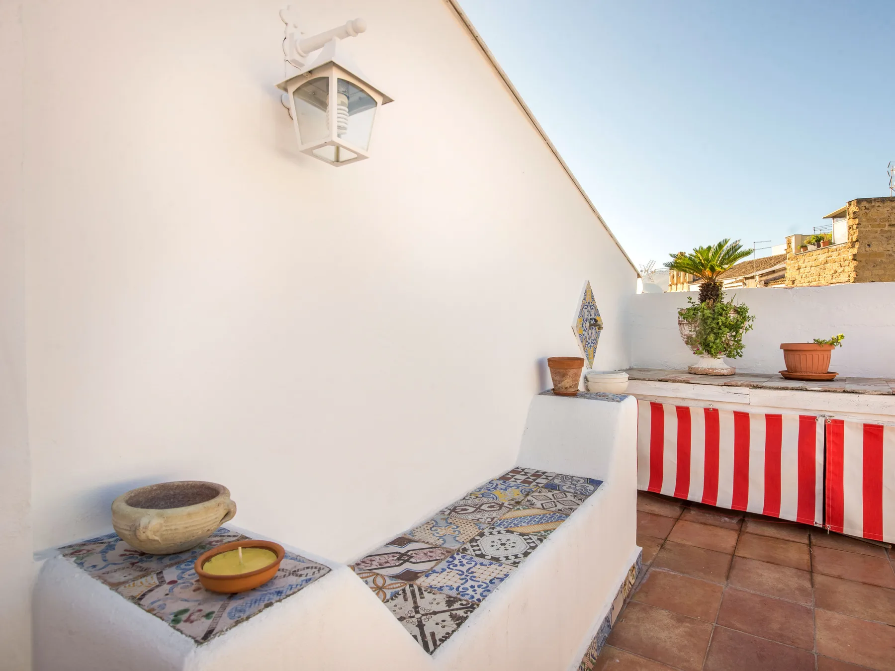 A sunny rooftop terrace with a tiled built-in bench and striped fabric screen.
