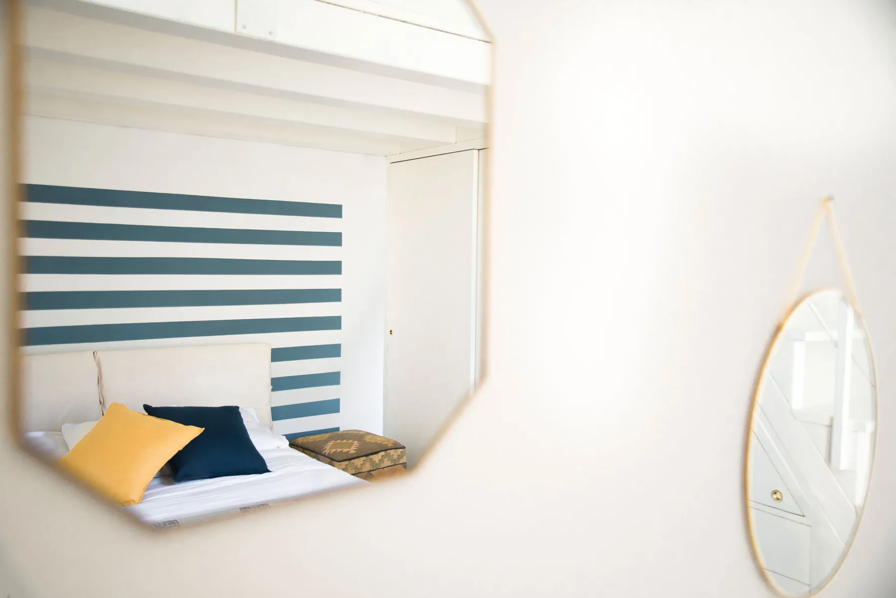 A bedroom with a bed, striped wall, and oval mirror.