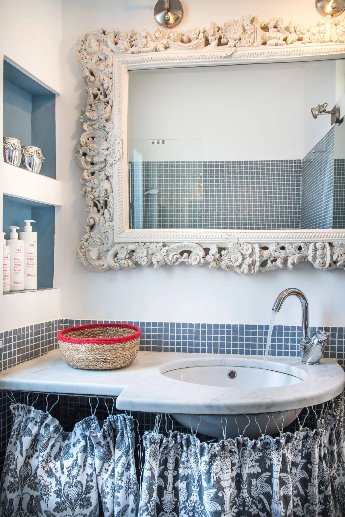 A bathroom vanity with a sink, patterned curtain, and ornate mirror.