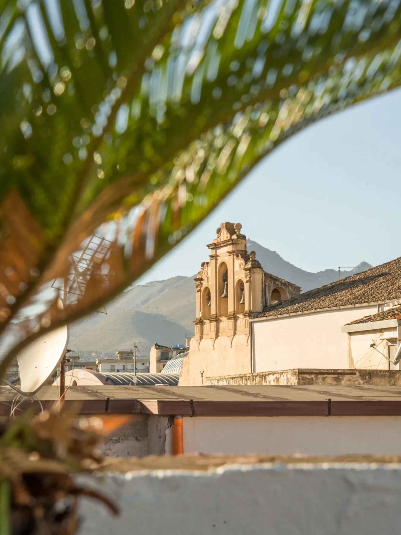A historic church tower rises above nearby rooftops, with mountains in the background.