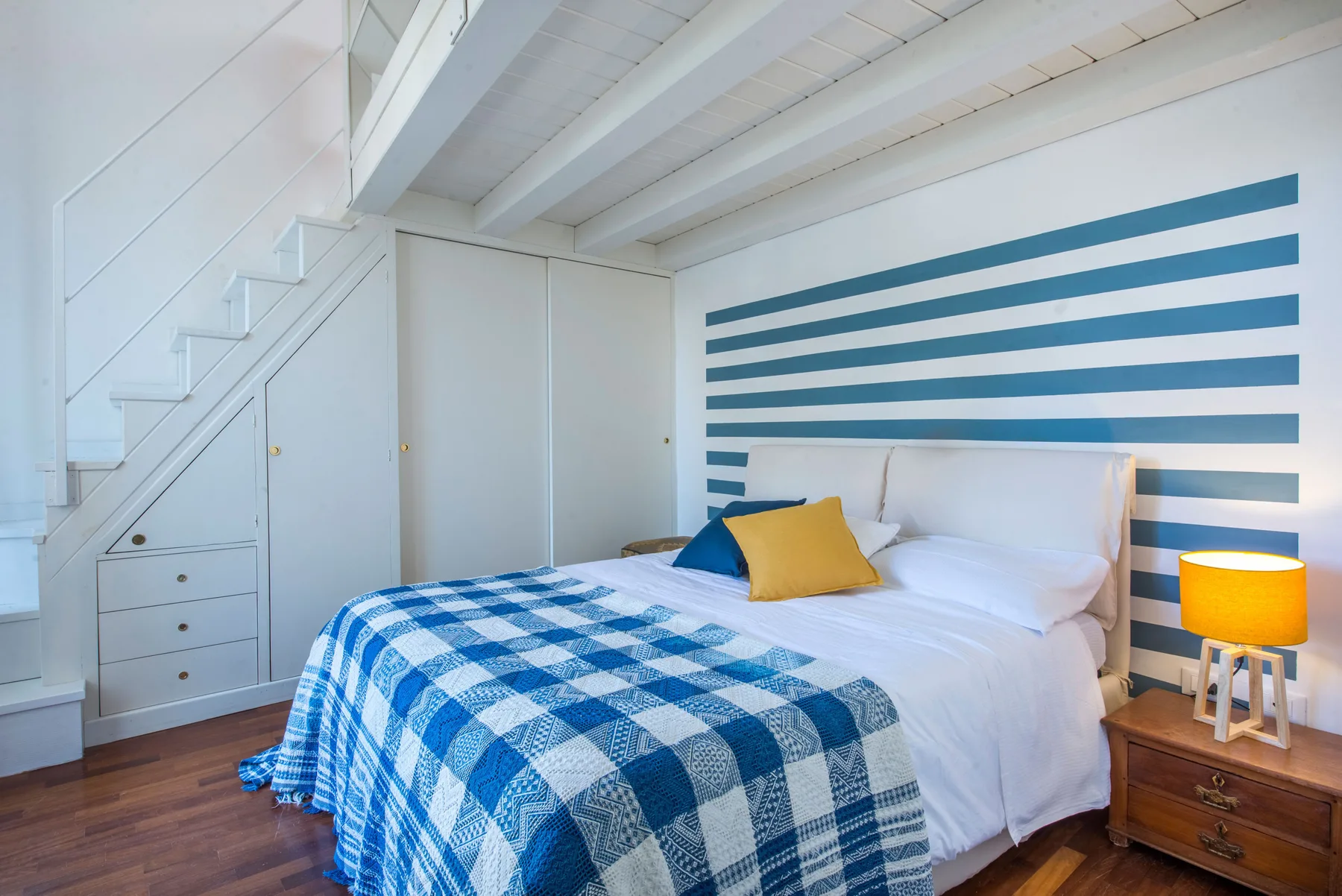 A bedroom with a bed beneath a blue-and-white striped wall.