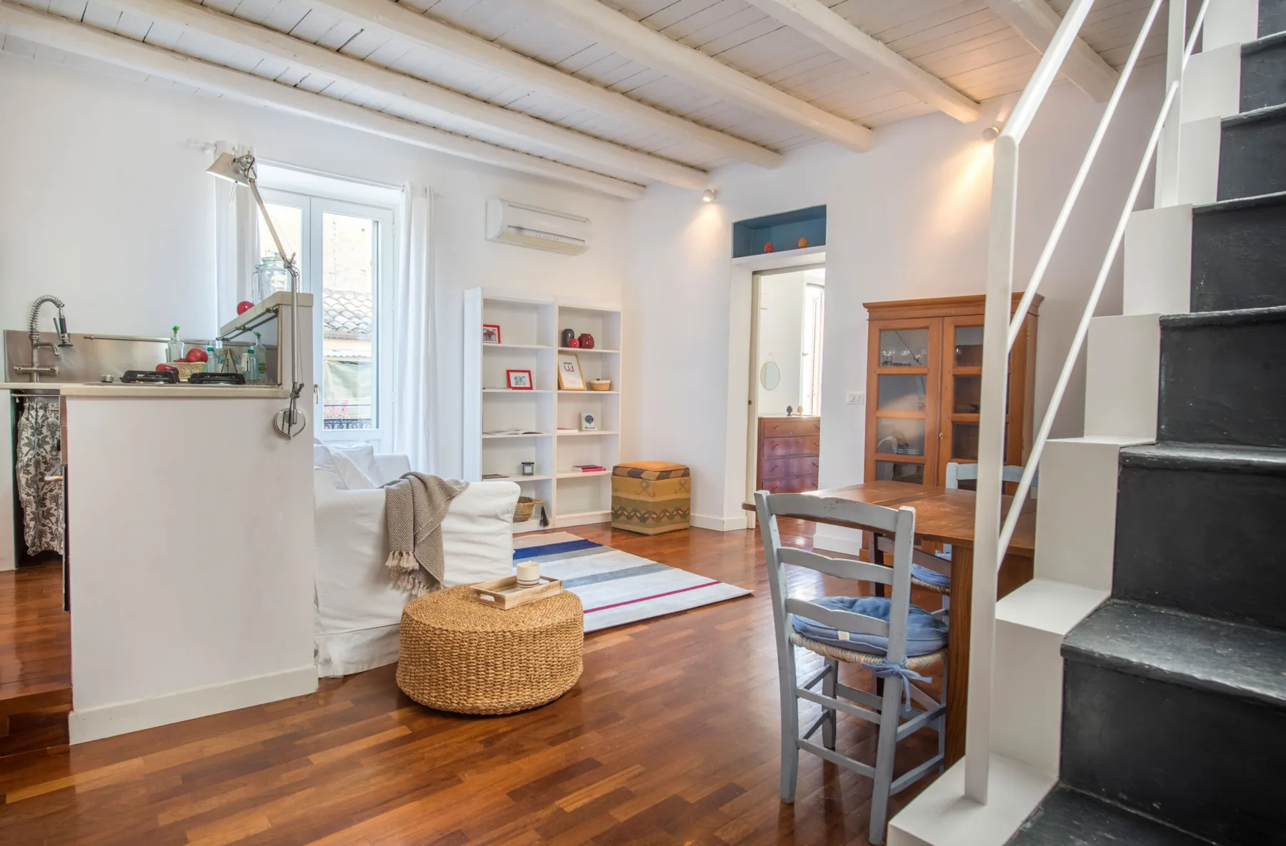 A bright living area with seating, a small table, and a staircase.