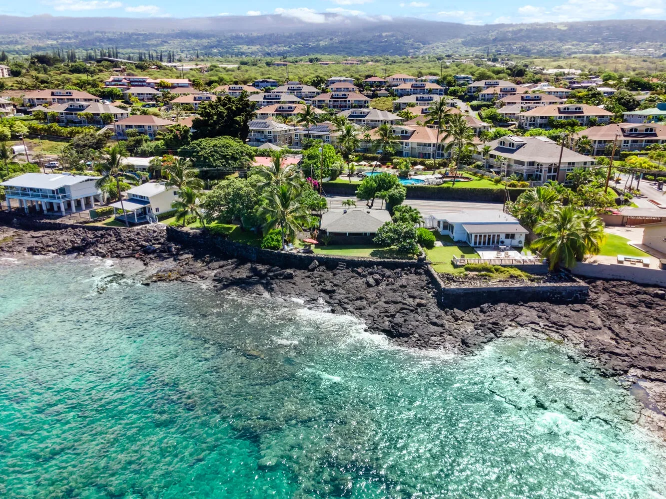 Vista aérea de casas costeras junto a una costa rocosa y aguas turquesas.