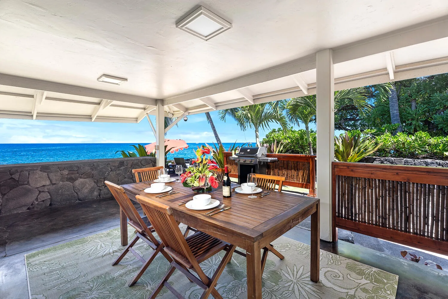 Una zona de comedor exterior cubierta da al océano, con una mesa de madera y sillas.