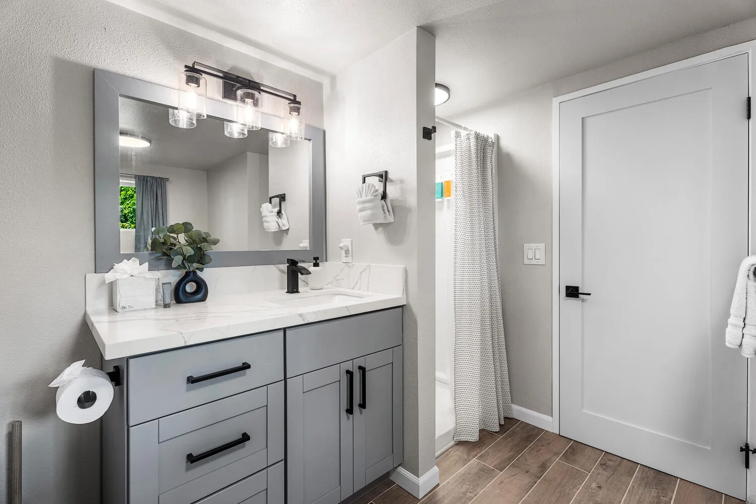 Un tocador de baño con espejo y una cortina de ducha junto a la puerta.