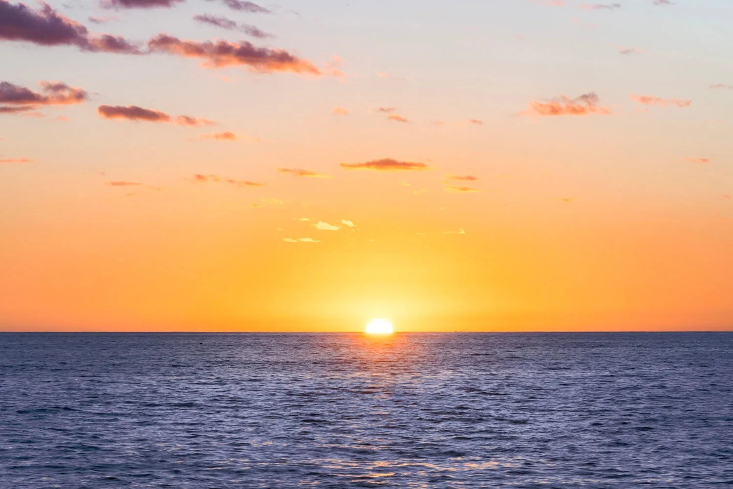El sol se pone sobre el océano bajo un cielo surcado de nubes.