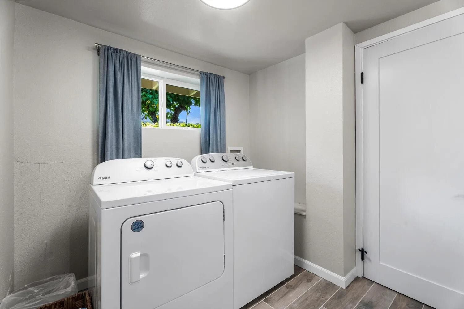 Un cuarto de lavandería con lavadora y secadora bajo una ventana con cortinas.