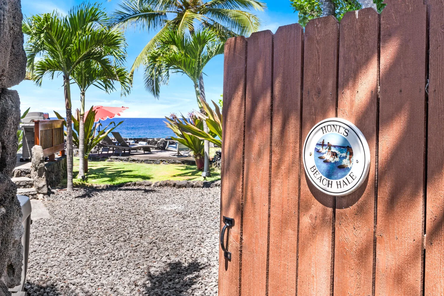 Una puerta de madera da a una escena tropical frente al mar, con palmeras.