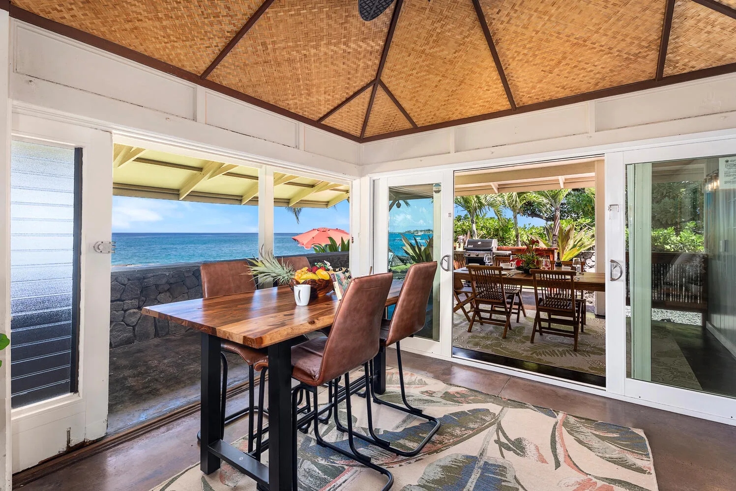 Un comedor abierto da al océano, con una mesa de madera y sillas.