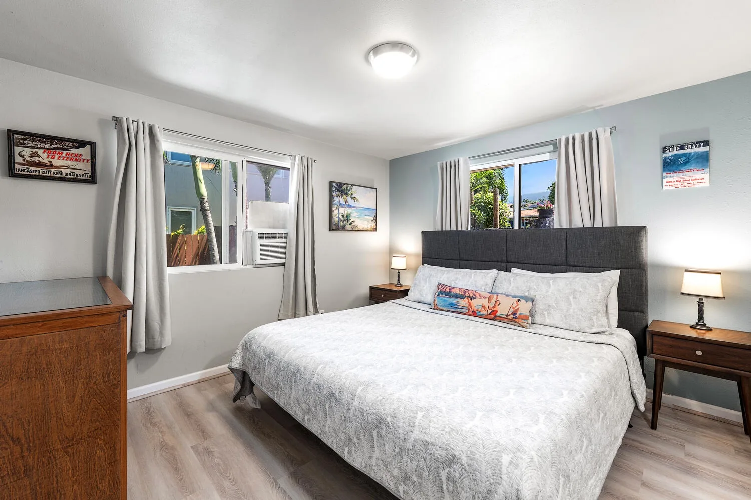 Un dormitorio con una cama grande, mesitas de noche y ventanas con cortinas claras.
