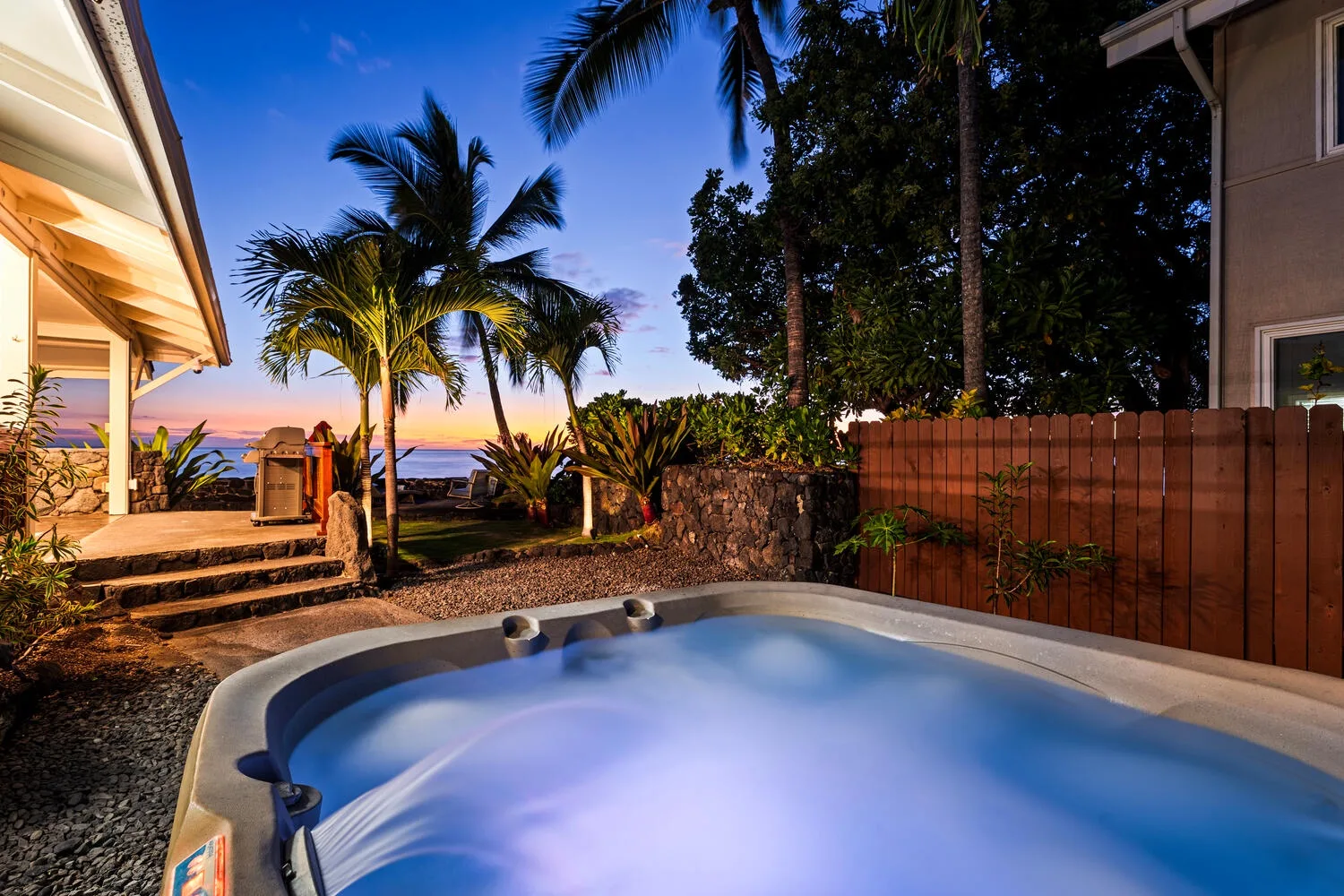 Un jacuzzi al aire libre está junto a un jardín tropical al anochecer.