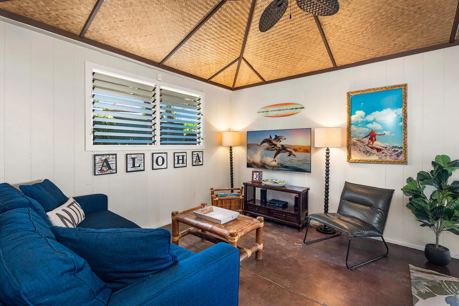 Una sala de estar con asientos azules, una mesa de centro de madera y arte tropical en las paredes.