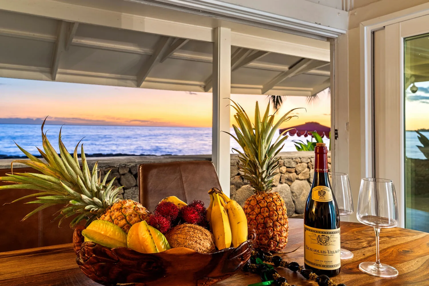 Una mesa con fruta, vino y copas está junto a una vista abierta del océano.