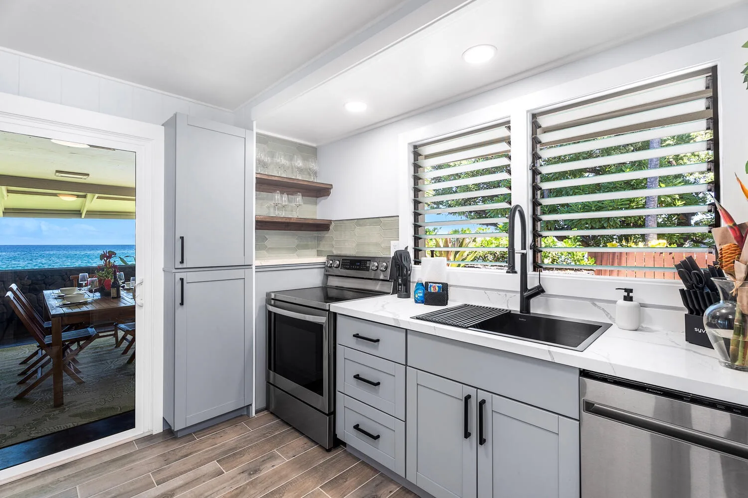 Una cocina luminosa con gabinetes blancos, encimeras oscuras y ventanas con vista al jardín.