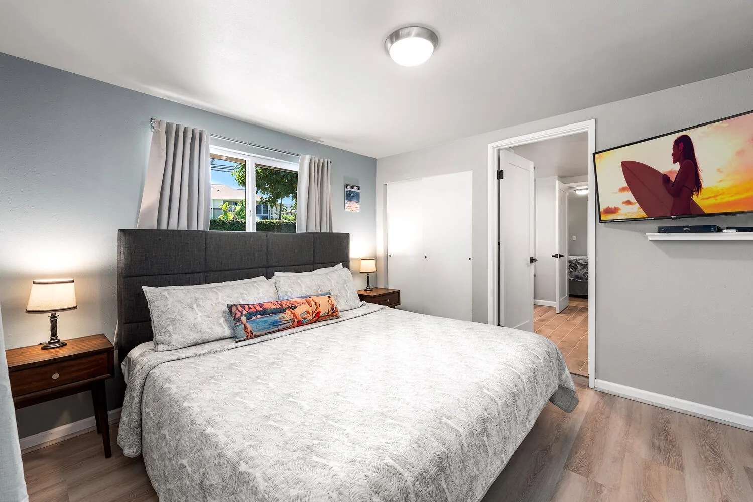 Un dormitorio con una cama, mesitas de noche y un televisor montado en la pared.