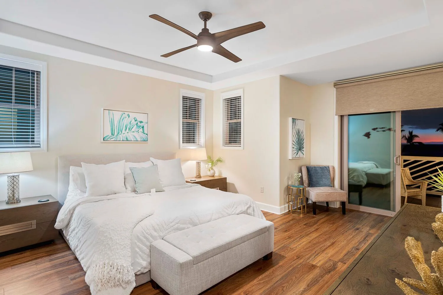 A bright bedroom features a large bed, bedside tables, and a ceiling fan.