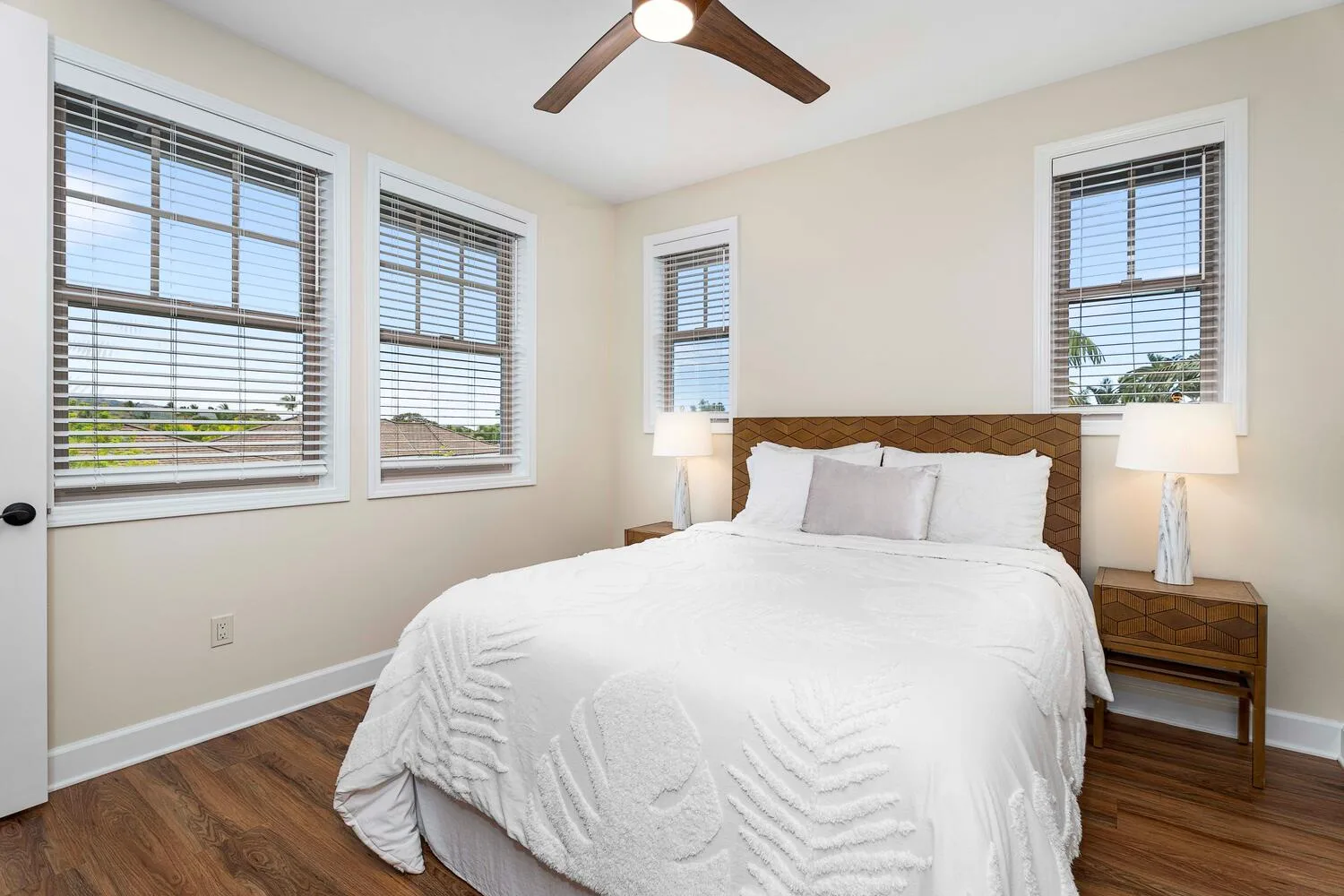 A bright bedroom with a large bed, bedside tables, and several windows.