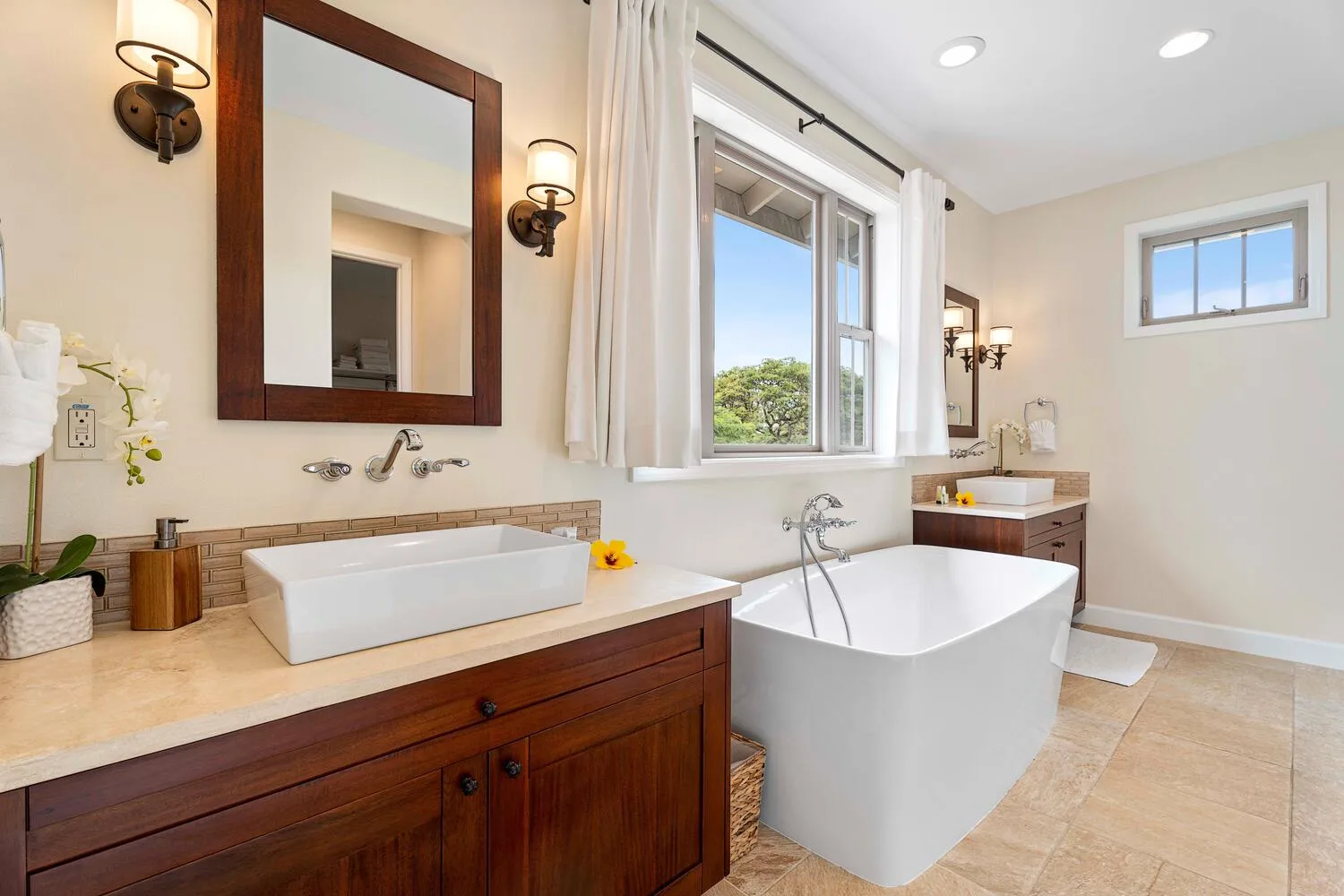 A bright bathroom features a freestanding tub, a vanity, and a large window.
