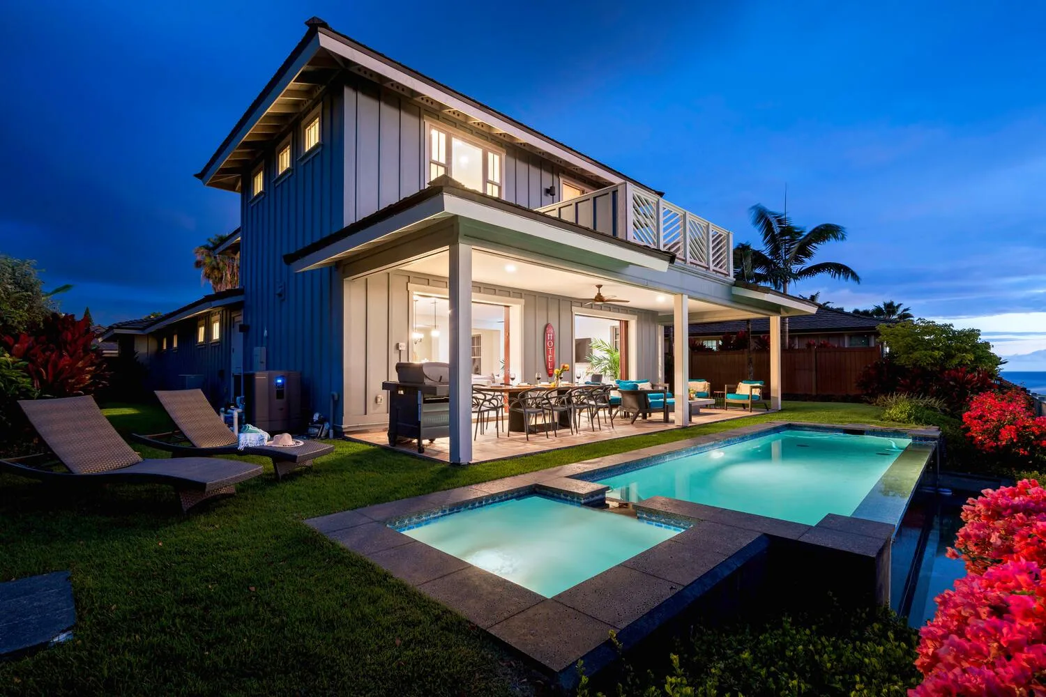 A modern two-story house opens onto a brightly lit patio and swimming pool.