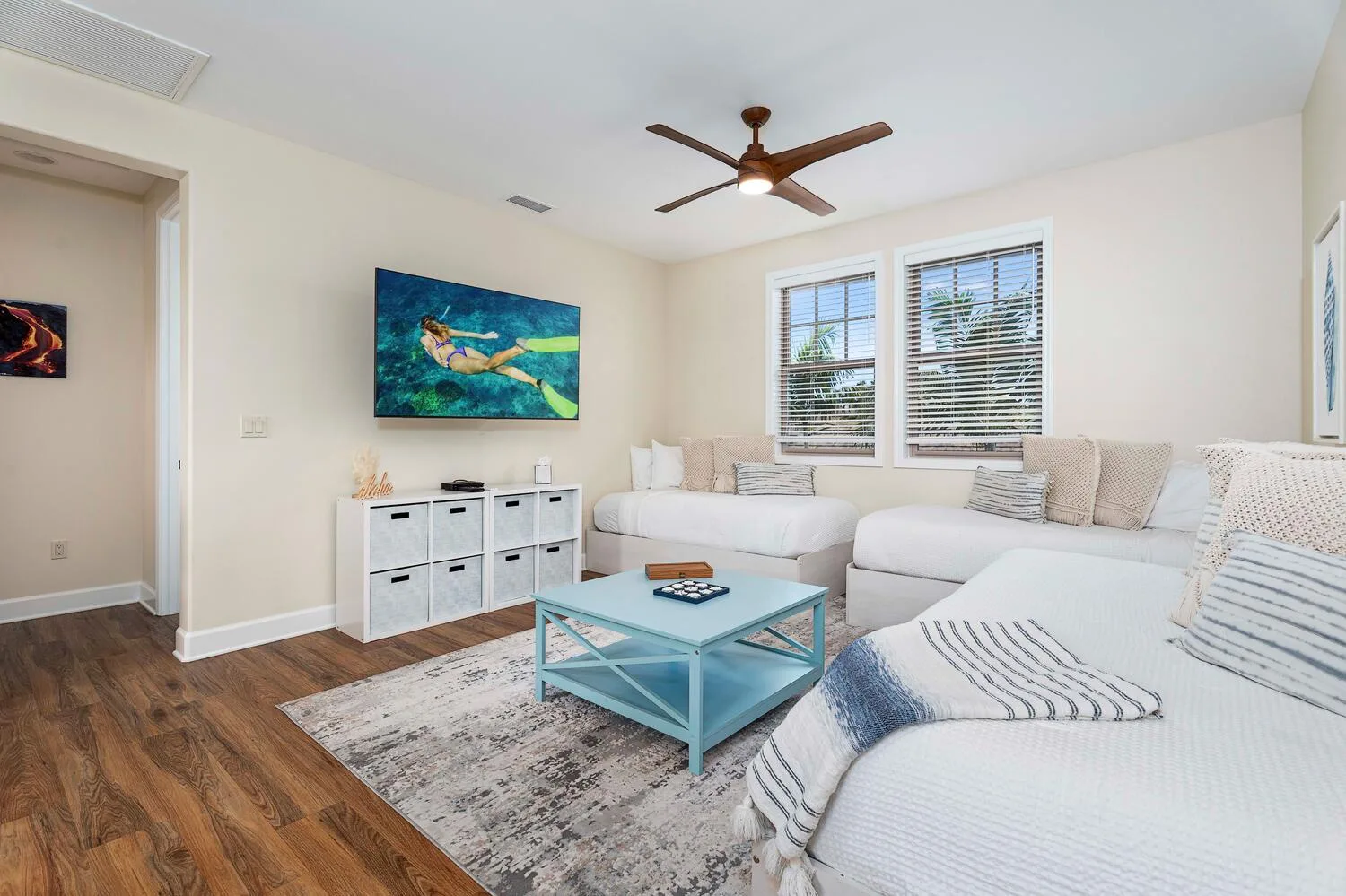 A bright living room with sectional seating, a coffee table, and windows with blinds.