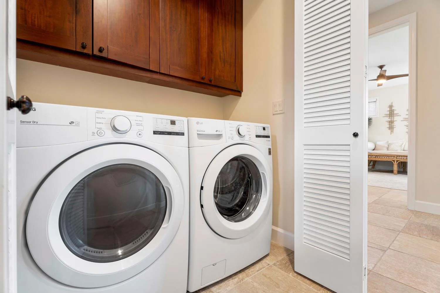 A laundry area with two front-loading machines beneath wooden cabinets.