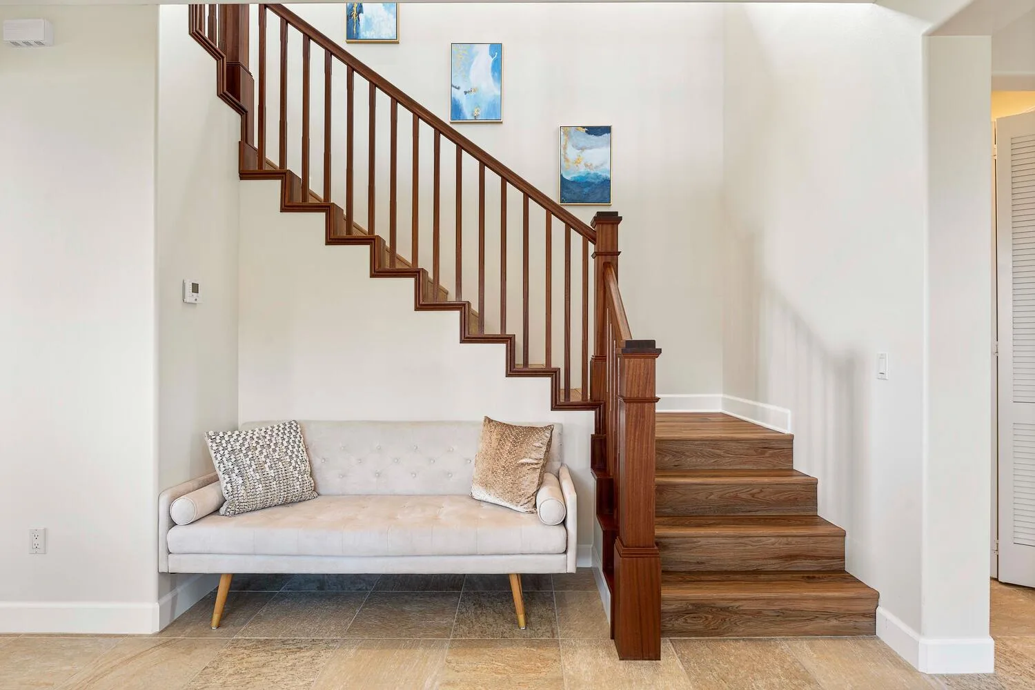 A bright living room with a pale sofa beside a wooden staircase.