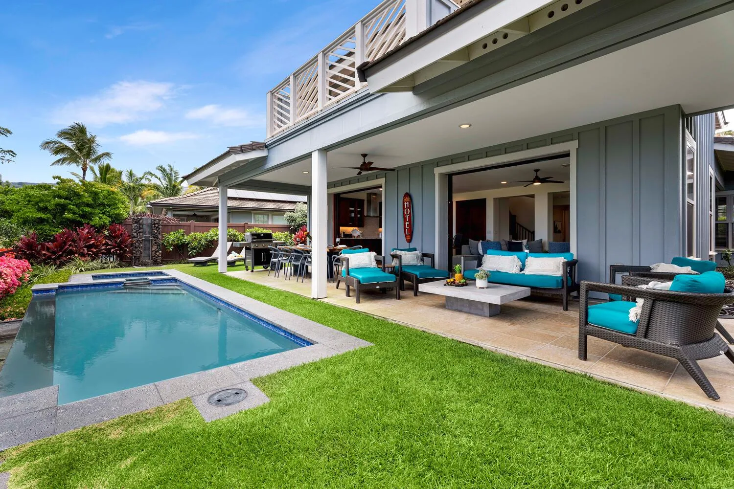 A patio with outdoor seating overlooks a swimming pool and green lawn.