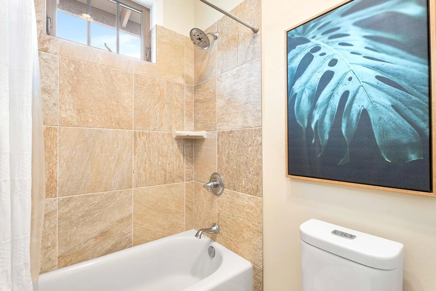 A tiled bathroom with a bathtub, shower fixtures, and framed botanical artwork.
